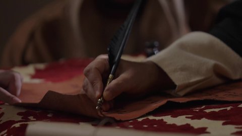 Pride in the authenticity of the Kingdom, wearing traditional dress on the national occasion, a close-up of a Saudi Arabian Gulf man wearing a ghutra, golden agal and bisht holding a pen in his hand writing on a historical leather manuscript, heritage letters and correspondence for the establishment of the first state in 1727 AD, the day we began, February 22