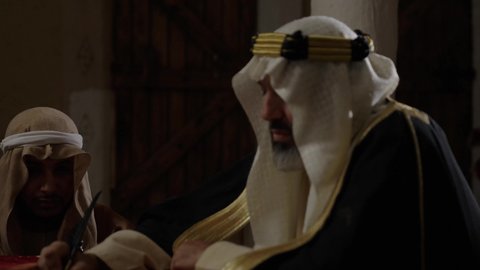 ارتداء الزي الشعبي في المناسبة الوطنية، الخطابات والمراسلات التراثية لتأسيس الدولة السعودية الأولى 1727م، يوم بدينا 22 فبراير,  الفخر بأصالة المملكة، تصوير مقرب لرجل عربي خليجي سعودي يرتدي الغترة والعقال الذهبي والبشت يقوم بتسليم مخطوطة جلد تاريخية إلى شخص آخر