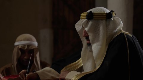ارتداء الزي الشعبي في المناسبة الوطنية، الخطابات والمراسلات التراثية لتأسيس الدولة السعودية الأولى 1727م، يوم بدينا 22 فبراير,  الفخر بأصالة المملكة، تصوير مقرب لرجل عربي خليجي سعودي يرتدي الغترة والعقال الذهبي والبشت يقوم بتسليم مخطوطة جلد تاريخية إلى شخص آخر