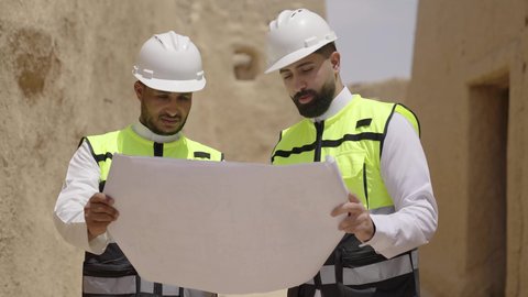 دراسة فن العمارة القديم واساسيات بناء البيوت الطينية، مهندسان عربيان خليجيان سعوديان يرتديان السترة وخوذة الحماية يقفان على اطلال قصر سلوى في البجيري الدرعية، يوم بدينا 1727 م، ذكرى تأسيس الدولة السعودية الأولى 22 فبراير