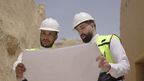 اكتشاف فن العمارة القديم واساسيات بناء البيوت الطينية، مهندسان عربيان خليجيان سعوديان يرتديان السترة وخوذة الحماية يقفان على اطلال قصر سلوى في البجيري الدرعية، يوم بدينا 1727 م، ذكرى تأسيس الدولة السعودية الأولى 22 فبراير