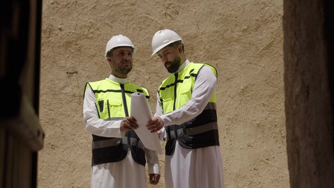 مهندسان عربيان خليجيان سعوديان يرتديان السترة وخوذة الحماية يقفان على اطلال قصر سلوى في البجيري الدرعية، يوم بدينا 1727 م، ذكرى تأسيس الدولة السعودية الأولى 22 فبراير، دراسة فن العمارة القديم واساسيات بناء البيوت الطينية