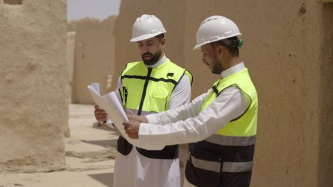 اكتشاف فن العمارة القديم واساسيات بناء البيوت الطينية، مهندسان عربيان خليجيان سعوديان يرتديان السترة وخوذة الحماية يقفان على اطلال قصر سلوى في البجيري الدرعية، يوم بدينا 1727 م، ذكرى تأسيس الدولة السعودية الأولى 22 فبراير