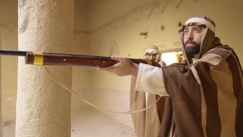 مفهوم المراقبة والحراسة، الدفاع والحفاظ على تاريخ وتراث المملكة، يوم بدينا 22 فبراير، الحرب والقتال بالبنادق لحماية الوطن، تأسيس الدولة السعودية الأولى 1727 م، رجل عربي خليجي سعودي يرتدي الزي الشعبي التقليدي يحمل البندقية في احياء شعبية طينية