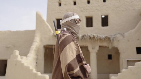 الحفاظ والدفاع على تاريخ وتراث المملكة، يوم بدينا 22 فبراير، الحرب والقتال بالبنادق لحماية الوطن، تأسيس الدولة السعودية الأولى 1727 م، رجل عربي خليجي سعودي يرتدي الزي الشعبي التقليدي يحمل البندقية في احياء شعبية طينية، مفهوم المراقبة والحراسة