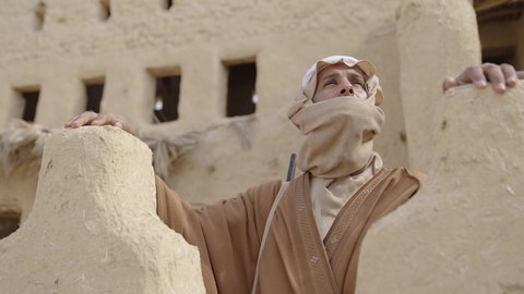 الحفاظ والدفاع على تاريخ وتراث المملكة، يوم بدينا 22 فبراير، الحرب والقتال بالبنادق لحماية الوطن، تأسيس الدولة السعودية الأولى 1727 م، رجل عربي خليجي سعودي يرتدي الزي الشعبي التقليدي يحمل البندقية في احياء شعبية طينية، مفهوم المراقبة والحراسة