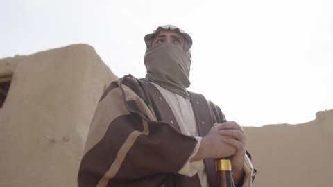 الدفاع والحفاظ على تاريخ وتراث المملكة، يوم بدينا 22 فبراير، الحرب والقتال بالبنادق لحماية الوطن، تأسيس الدولة السعودية الأولى 1727 م، رجل عربي خليجي سعودي يرتدي الزي الشعبي التقليدي يحمل البندقية في احياء شعبية طينية، مفهوم المراقبة والحراسة