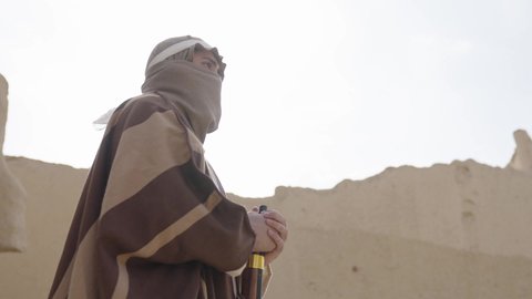 Preserving and defending the history and heritage of the Kingdom, the day we began, February 22, war and fighting with guns to protect the homeland, the establishment of the first Saudi state in 1727 AD, a Saudi Gulf Arab man wearing traditional folk costume carrying a gun in a mud-brick neighborhood, the concept of surveillance and guarding