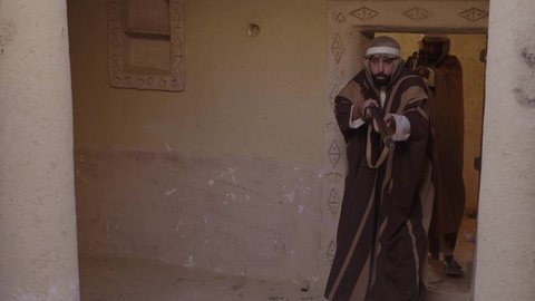 الدفاع والحفاظ على تاريخ وتراث المملكة، يوم بدينا 22 فبراير، الحرب والقتال بالبنادق لحماية الوطن، تأسيس الدولة السعودية الأولى 1727 م، رجل عربي خليجي سعودي يرتدي الزي الشعبي التقليدي يحمل البندقية في احياء شعبية طينية، مفهوم المراقبة والحراسة