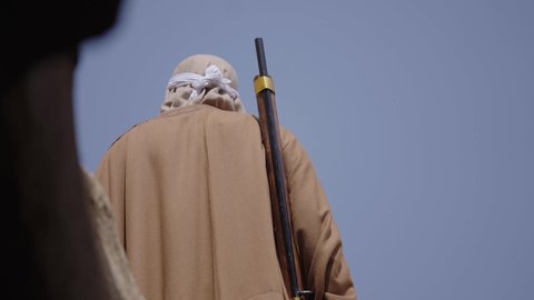 Defending and preserving the history and heritage of the Kingdom, the day we began, February 22, war and fighting with guns to protect the homeland, the establishment of the first Saudi state in 1727 AD, a Saudi Gulf Arab man wearing traditional folk costume carrying a gun in a mud-brick neighborhood, the concept of surveillance and guarding