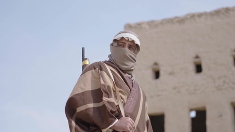 الحرب والقتال بالبنادق لحماية الوطن، تأسيس الدولة السعودية الأولى 1727 م، رجل عربي خليجي سعودي يرتدي الزي الشعبي التقليدي يحمل البندقية في احياء شعبية طينية، مفهوم المراقبة والحراسة، الحفاظ والدفاع على تاريخ وتراث المملكة، يوم بدينا 22 فبراير