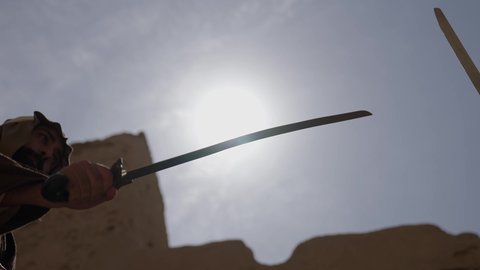 المبارزة بالسيف للحماية وتأسيس الدولة السعودية الأولى 1727 م، رجلان عربيان خليجيان سعوديان يرتديان الزي الشعبي يتبارزان بالسيوف في بيت طيني، يوم بدينا 22 فبراير، مفهوم الحرب والدفاع عن الوطن، الحفاظ على تاريخ وتراث المملكة، أدوات الحرب القديمة