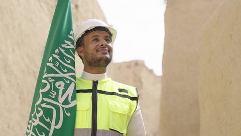 رفع علم المملكة في الأماكن التراثيه الشعبيه في 11 مارس، فن العمارة القديم وبناء البيوت الطينية، مهندس عربي خليجي سعودي مبتسم يرتدي السترة وخوذة الحماية بايماءات الفخر والاعتزاز في اليوم الوطني 23 سبتمبر، يوم بدينا 1727 م، ذكرى تأسيس الدولة السعودية الأولى 22 فبراير