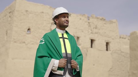 ذكرى تأسيس الدولة السعودية الأولى 22 فبراير، رفع علم المملكة في الأماكن التراثيه الشعبيه في 11 مارس، فن العمارة القديم وبناء البيوت الطينية، مهندس عربي خليجي سعودي مبتسم يرتدي السترة وخوذة الحماية بايماءات الفخر والاعتزاز في اليوم الوطني 23 سبتمبر، يوم بدينا 1727 م