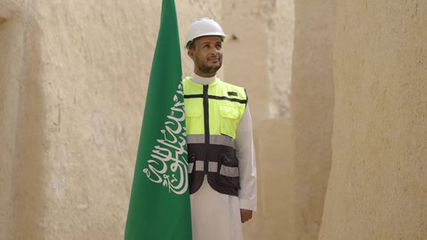 رفع علم المملكة في الأماكن التراثيه الشعبيه في 11 مارس، فن العمارة القديم وبناء البيوت الطينية، مهندس عربي خليجي سعودي مبتسم يرتدي السترة وخوذة الحماية بايماءات الفخر والاعتزاز في اليوم الوطني 23 سبتمبر، يوم بدينا 1727 م، ذكرى تأسيس الدولة السعودية الأولى 22 فبراير