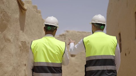 تبادل الاحاديث حول اكتشاف فن العمارة القديم، مهندسان عربيان خليجيان سعوديان يرتديان السترة وخوذة الحماية ينظران الى اساسيات بناء البيوت الطينية، يوم بدينا 1727 م، ذكرى تأسيس الدولة السعودية الأولى 22 فبراير