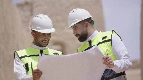 يوم بدينا 1727 م، ذكرى تأسيس الدولة السعودية الأولى 22 فبراير، تبادل الاحاديث حول اكتشاف فن العمارة القديم، مهندسان عربيان خليجيان سعوديان يرتديان السترة وخوذة الحماية ينظران الى اساسيات بناء البيوت الطينية