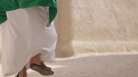 فن العمارة القديم وبناء البيوت الطينية، يوم العلم 11 مارس, إحياء ذكرى اليوم الوطني السعودي 23 سبتمبر, إيماءات الفخر و السرور بالانتماء للوطن, رجل عربي خليجي سعودي مبتسم يرتدي الشماغ و الثوب التقليدي يقف في بيت طيني ويحمل بيده علم المملكة، يوم بدينا 1727 م