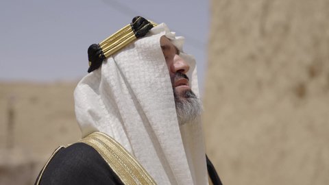 إحياء ذكرى تأسيس الدولة السعودية الأولى 1727 م, يوم بدينا 22 فبراير, رجل عربي خليجي سعودي يرتدي البشت والغترة والعقال الذهبي العريض يقف أمام منزل طيني قديم، مفهوم حب الوطن والانتماء اليه، قرية تاريخية قديمة، ارتداء الزي الشعبي  التقليدي في عيد ومناسبة وطنية