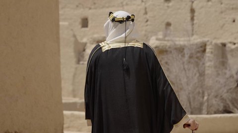 قرية تاريخية قديمة، ارتداء الزي الشعبي  التقليدي في عيد ومناسبة وطنية، إحياء ذكرى تأسيس الدولة السعودية الأولى 1727 م, يوم بدينا 22 فبراير, رجل عربي خليجي سعودي يرتدي البشت والغترة والعقال الذهبي العريض يقف أمام منزل طيني قديم، مفهوم حب الوطن والانتماء اليه