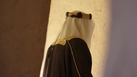 مفهوم حب الوطن والانتماء اليه، قرية تاريخية قديمة، ارتداء الزي الشعبي  التقليدي في عيد ومناسبة وطنية، إحياء ذكرى تأسيس الدولة السعودية الأولى 1727 م, يوم بدينا 22 فبراير, رجل عربي خليجي سعودي يرتدي البشت والغترة والعقال الذهبي العريض يقف أمام منزل طيني قديم