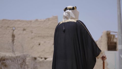 ارتداء الزي الشعبي لإحياء عيد ومناسبة وطنية، قرية تاريخية قديمة، إحياء ذكرى تأسيس الدولة السعودية الأولى 1727 م, يوم بدينا 22 فبراير, رجل عربي خليجي سعودي يرتدي البشت والغترة والعقال الذهبي العريض يتجول في الأحياء القديمة، مفهوم حب الوطن والانتماء اليه