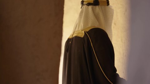 يوم بدينا 22 فبراير, رجل عربي خليجي سعودي يرتدي البشت والغترة والعقال الذهبي العريض يقف في منزل طيني قديم، مفهوم حب الوطن والانتماء اليه، قرية تاريخية قديمة، ارتداء الزي الشعبي  التقليدي في عيد ومناسبة وطنية، إحياء ذكرى تأسيس الدولة السعودية الأولى 1727 م