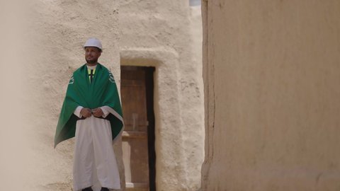 مهندس عربي خليجي سعودي مبتسم يرتدي السترة وخوذة الحماية بايماءات الفخر والاعتزاز في اليوم الوطني 23 سبتمبر، يوم بدينا 1727 م، ذكرى تأسيس الدولة السعودية الأولى 22 فبراير، رفع علم المملكة في الأماكن التراثيه الشعبيه في 11 مارس، فن العمارة القديم وبناء البيوت الطينية