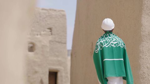 مهندس عربي خليجي سعودي مبتسم يرتدي السترة وخوذة الحماية بايماءات الفخر والاعتزاز في اليوم الوطني 23 سبتمبر، يوم بدينا 1727 م، ذكرى تأسيس الدولة السعودية الأولى 22 فبراير، رفع علم المملكة في الأماكن التراثيه الشعبيه في 11 مارس، فن العمارة القديم وبناء البيوت الطينية