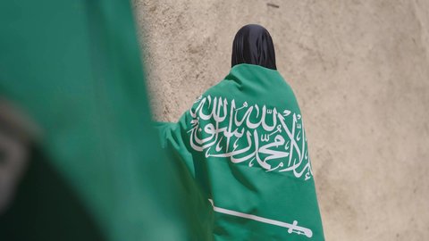 Old heritage mud houses, a symbol of national identity, a Saudi Arabian Gulf woman wearing a black abaya and burqa carrying the Kingdom's flag, celebrating the founding of the first Saudi state on February 22, the anniversary of the National Day on September 23, the day of our beginning in 1727 AD, wearing traditional folk costume