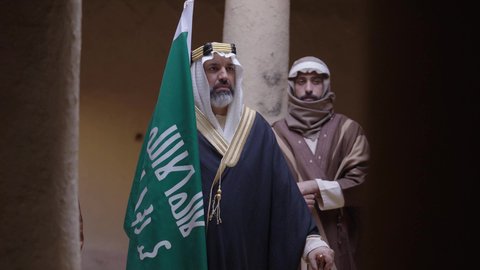 علم تأسيس المملكة العربية السعودية، إظهار الولاء والحب للوطن, مجموعة رجال عرب خليجون سعوديون يرتدون الزي الشعبي التقليدي في المناسبة الوطنية يقفون في بيت طيني قديم بإيماءات الشموخ والاعتزاز، ذكرى تأسيس الدولة السعودية الأولى 1727 م، يوم بدينا 22 فبراير