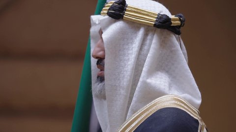 الاحتفال بيوم العلم السعودي11مارس، يوم بدينا22 فبراير, مفهوم حب الوطن والانتماء اليه, ذكرى تأسيس الدولة السعودية الأولى1727م, رجل عربي خليجي سعودي يرتدي البشت والغترة يقف في منزل طيني ويمسك علم يوم التأسيس بتعابير الشموخ، ارتداء الزي الشعبي في مناسبة وطنية