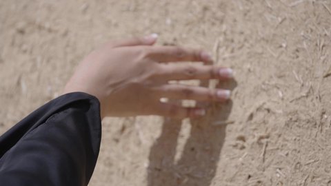 The Day We Began 1727 AD, the anniversary of the founding of the first Saudi state, February 22, a close-up of the hand of a Saudi Arabian Gulf woman wearing traditional dress touching a mud wall, traditional mud houses in the Kingdom of Saudi Arabia, pride in history