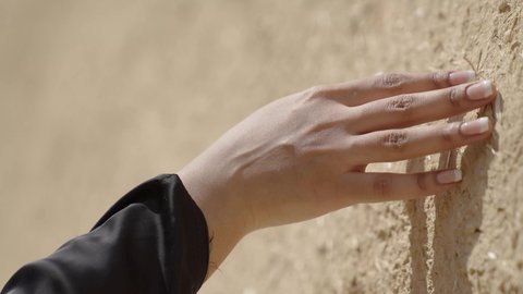 يوم بدينا 1727 م، ذكرى تأسيس الدولة السعودية الاولى 22 فبراير، تصوير مقرب ليد امرأة عربية خليجية سعودية ترتدي الزي الشعبي تقوم بلمس جدار من الطين، البيوت الطينية التراثية في المملكة العربية السعودية، الاعتزاز والفخر بالتاريخ