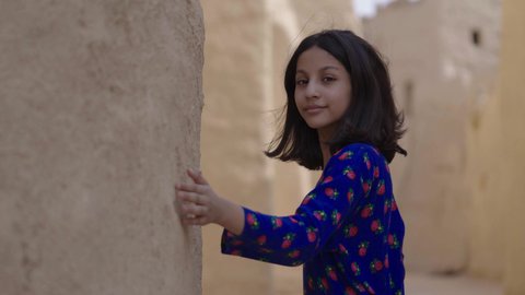 المحافظة على التراث السعودي، تربيه الأبناء على حب الوطن، يوم بدينا 1727 م، ذكرى تأسيس الدولة السعودية الاولى 22 فبراير، تصوير مقرب لفتاة عربيه خليجية سعودية مبتسمة ترتدي الزي التقليدي الشعبي تتجول في منزل طيني، الاحتفال بالمناسبات والأعياد الوطنية بإيماءات السعادة