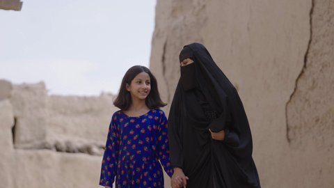 تربيه الأبناء على حب الوطن، يوم بدينا 1727 م، ذكرى تأسيس الدولة السعودية الاولى 22 فبراير، إمرأة عربية خليجية سعودية ترتدي البرقع والعباءة تتجول مع ابنتها في حي طيني شعبي، المحافظة على التراث السعودي، تبادل الأحاديث بإيماءات السعادة