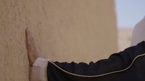 احياء ذكرى تأسيس الدولة السعودية الاولى 22 فبراير، تصوير مقرب ليد رجل عربي خليجي سعودي رتدي الزي الشعبي يقوم بلمس جدار من الطين، البيوت الطينية التراثية، يوم بدينا 1727 م