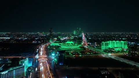 Transportation and traffic movement on the main streets and roads in the Kingdom of Saudi Arabia, aerial drone footage of organized traffic in the capital, the growth and development of infrastructure, and towers lit up in green to celebrate Saudi National Day in Riyadh.