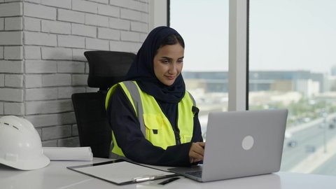 استخدام الوسائل التقنية الحديثة، تحقيق أهداف الشركة، مهندسة عربية سعودية خليجية محجبة ترتدي سترة الحماية تقوم بتدوين الملاحظات والمعلومات، العمل على جهاز الحاسوب المحمول بإيماءات الاندماج والتركيز،  إنجاز المهام اليومية في المكتب, مهن ووظائف نسائية سعودية.