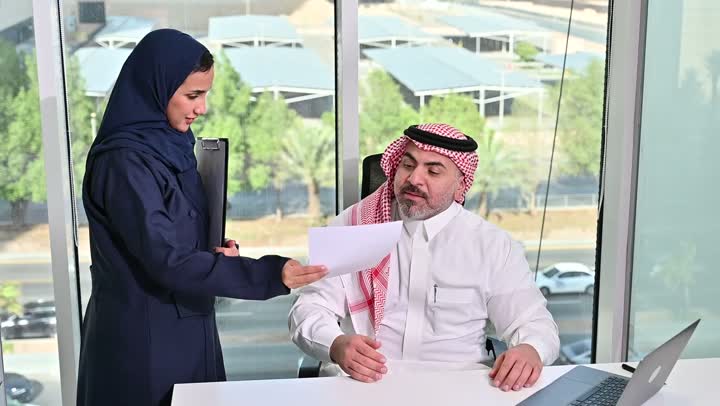 ايماءات التركيز والاندماج، مهنة ووظيفة مكتبية سعودية، كتابة وتدوين البيانات والنتائج، ادارة وانجاز المهام باستخدام جهاز تقني حديث ومتطور, تصوير مقرب لرجل عربي خليجي سعودي يرتدي الشماغ والثوب التقليدي يعمل على الحاسوب المحمول