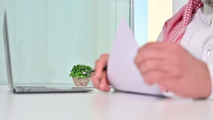 Saudi office profession and job, writing and recording data and results, managing and completing tasks using a modern and advanced technical device, close-up of a Saudi Arabian Gulf man wearing a traditional shemagh and thobe working on a laptop, gestures of concentration and integration