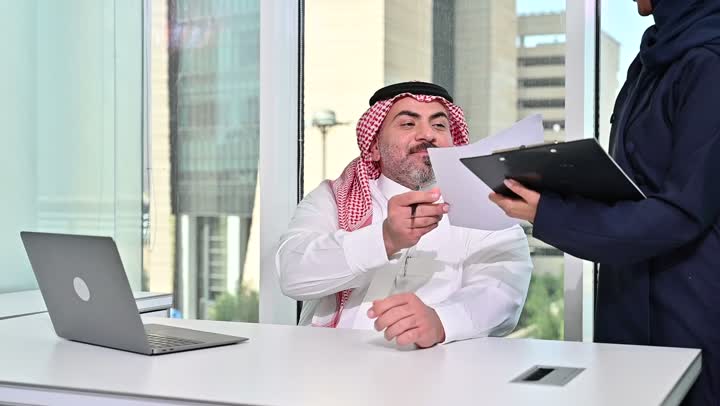 العمل على الحاسوب المحمول، مهنة ووظيفة مكتبية سعودية، كتابة وتدوين البيانات والنتائج، ادارة وانجاز المهام باستخدام جهاز تقني حديث ومتطور, تصوير مقرب لرجل عربي خليجي سعودي يرتدي الشماغ والثوب التقليدي وتقف بجانبه السكرتيرة