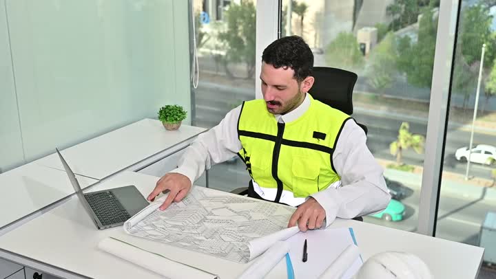 العمل على الحاسوب المحمول، الاهتمام بالتطور العمراني بسواعد المهندسين السعوديين, مهندس عربي خليجي سعودي يرتدي سترة العمل وخوذة الحماية البيضاء ينجز المهام اليومية في المكتب ، مفهوم الهندسة والإنشاءات المعمارية، مشاريع إعمارية سعودية وطنية