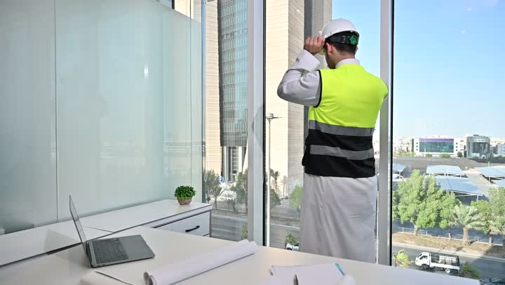 العمل على الحاسوب المحمول، الاهتمام بالتطور العمراني بسواعد المهندسين السعوديين, مهندس عربي خليجي سعودي يرتدي سترة العمل وخوذة الحماية البيضاء ينجز المهام اليومية في المكتب ، مفهوم الهندسة والإنشاءات المعمارية، مشاريع إعمارية سعودية وطنية