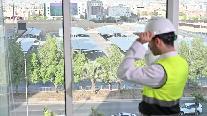 الاهتمام بالتطور العمراني بسواعد المهندسين السعوديين, مهندس عربي خليجي سعودي يرتدي سترة العمل وخوذة الحماية البيضاء ينجز المهام اليومية في المكتب، متابعة مخطط المشروع الهندسي وتدقيقه, مفهوم الهندسة والإنشاءات المعمارية، مشاريع إعمارية سعودية وطنية