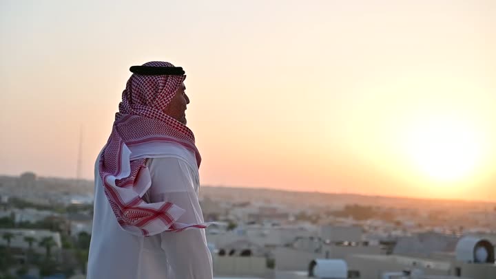 Concern for outward appearance, the concept of masculinity and elegance, a Saudi Arabian Gulf man wearing the traditional thobe and shemagh standing with gestures of joy and happiness, a background of towers and skyscrapers in Riyadh