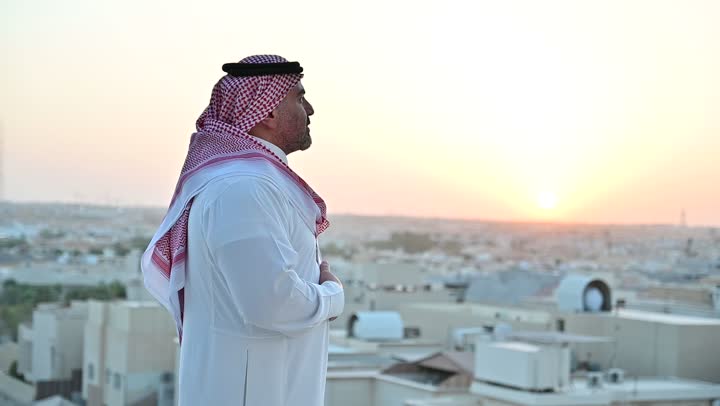 الاهتمام بالمظهر الخارجي، مفهوم الرجولة والأناقة، رجل عربي خليجي سعودي يرتدي الثوب التقليدي والشماغ يقف بإيماءات الفرح والسرور، خلفية الابراج وناطحات السحاب في الرياض