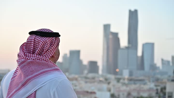 الاهتمام بالمظهر الخارجي، مفهوم الرجولة والأناقة، رجل عربي خليجي سعودي يرتدي الثوب التقليدي والشماغ يقف بإيماءات الفرح والسرور، خلفية الابراج وناطحات السحاب في الرياض