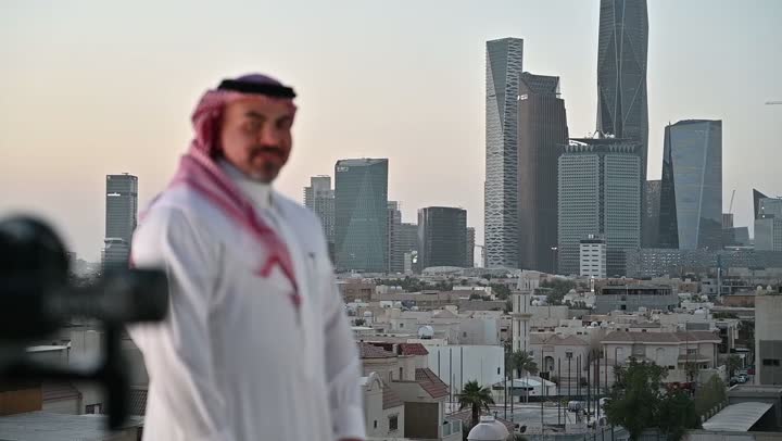 استخدام كاميرا رقمية عالية الدقة، إتقان واحتراف مهنة التصوير، الاهتمام بالمظهر الخارجي، مفهوم الرجولة والأناقة، مصور فوتوغرافي يقوم بتصوير رجل عربي خليجي سعودي يرتدي الثوب التقليدي والشماغ يقف بإيماءات الفرح والسرور، خلفية الابراج وناطحات السحاب في الرياض