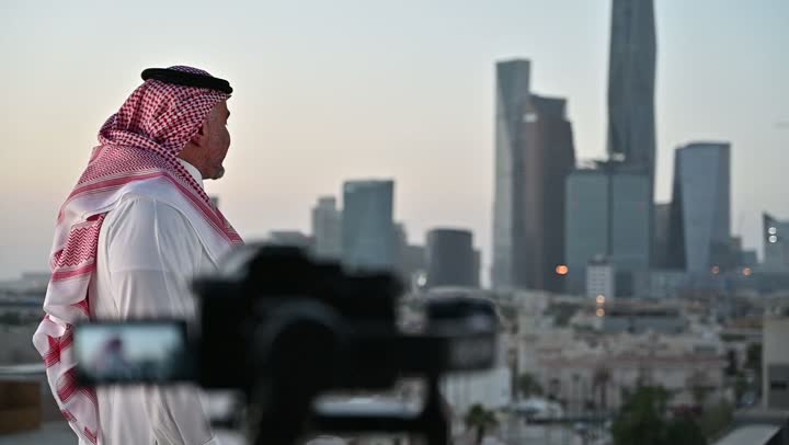 استخدام كاميرا رقمية عالية الدقة، إتقان واحتراف مهنة التصوير، الاهتمام بالمظهر الخارجي، مفهوم الرجولة والأناقة، مصور فوتوغرافي يقوم بتصوير رجل عربي خليجي سعودي يرتدي الثوب التقليدي والشماغ يقف بإيماءات الفرح والسرور، خلفية الابراج وناطحات السحاب في الرياض